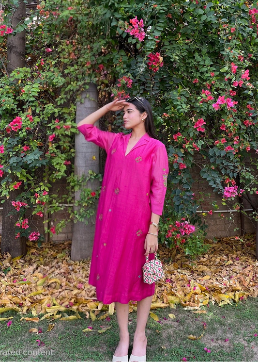 Woman in a pink dress standing in a garden with flowering plants and trees.