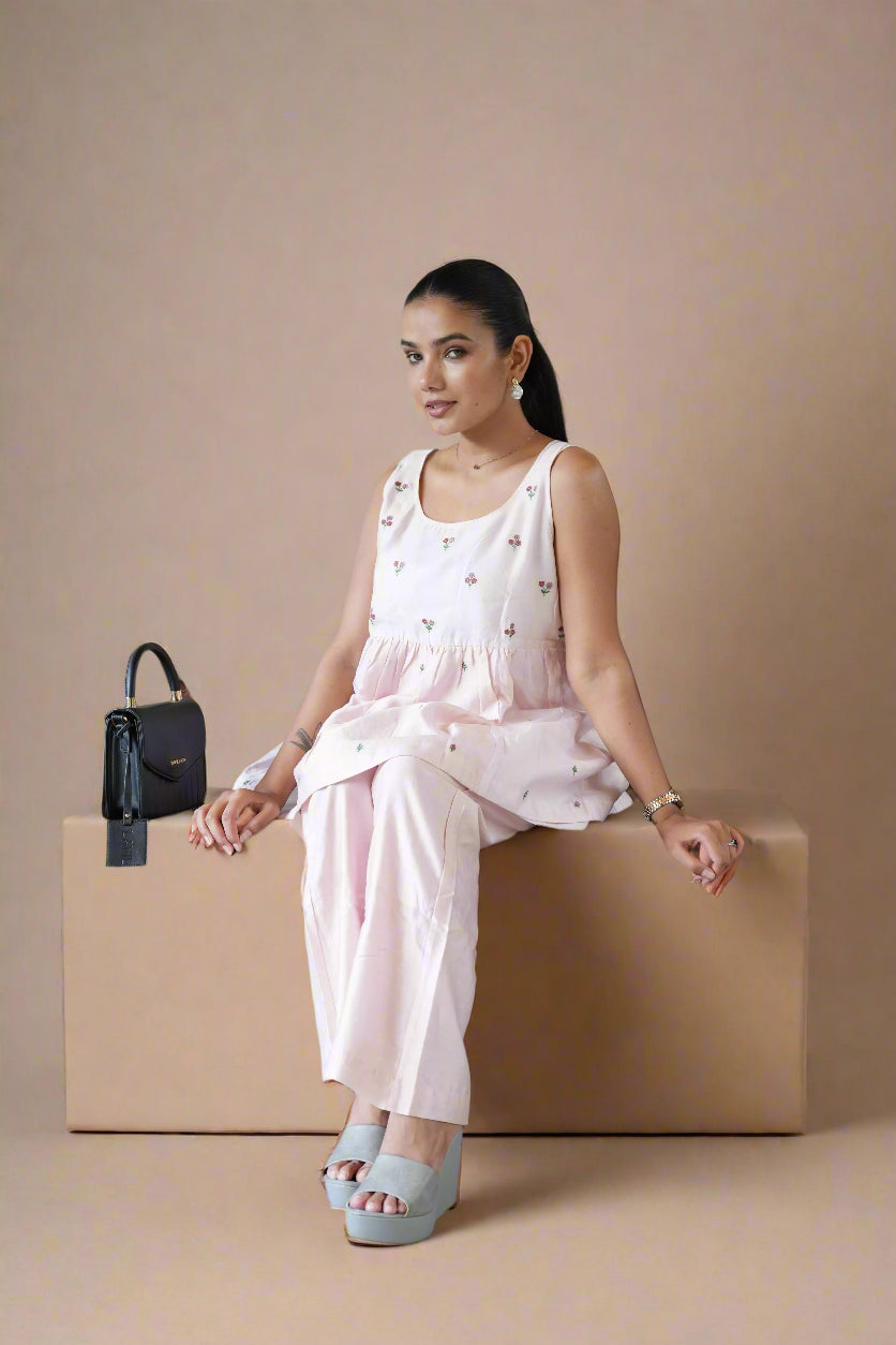 Woman in a light pink dress sitting on a beige box with a black handbag beside her.