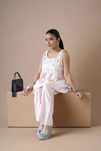 Woman in a light pink dress sitting on a beige box with a black handbag beside her.