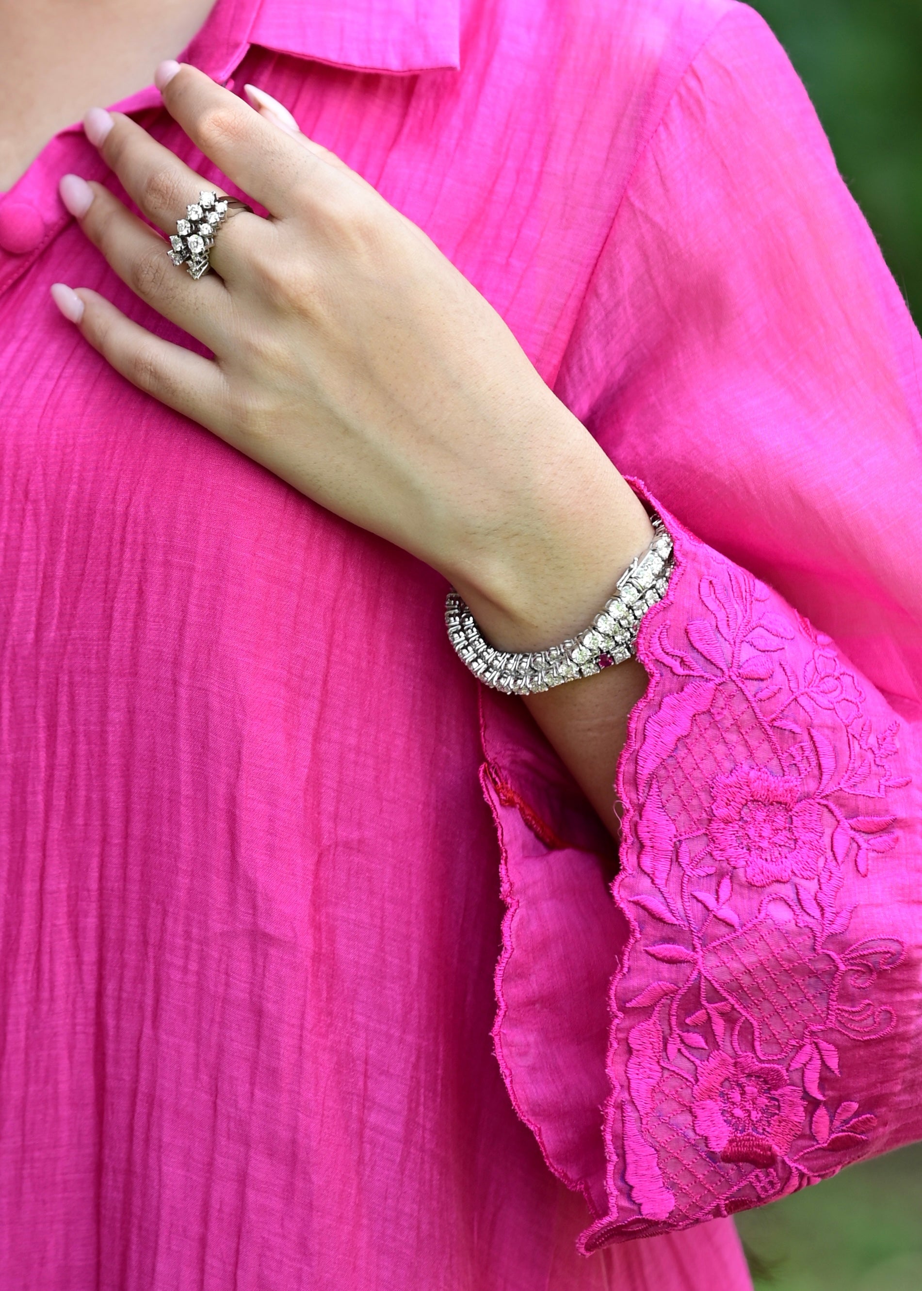 A close-up lifestyle shot of a person wearing a vibrant pink embroidered blouse, featuring a silver-toned diamond-encrusted ring on their finger and a matching diamond bracelet on their wrist.