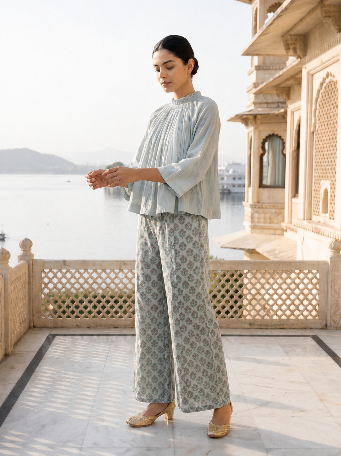 Woman in a light blue outfit standing on a balcony with a scenic view.