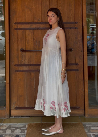 Woman in a white dress with floral patterns standing in front of a wooden door.