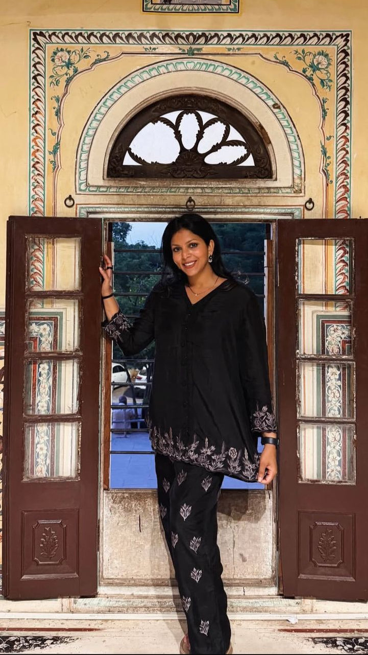 Woman standing in a decorative doorway with intricate patterns and a view of Nahargarh Fort in the background.